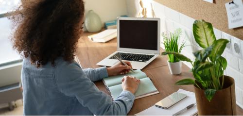 Girl writing on a book in front of a laptop